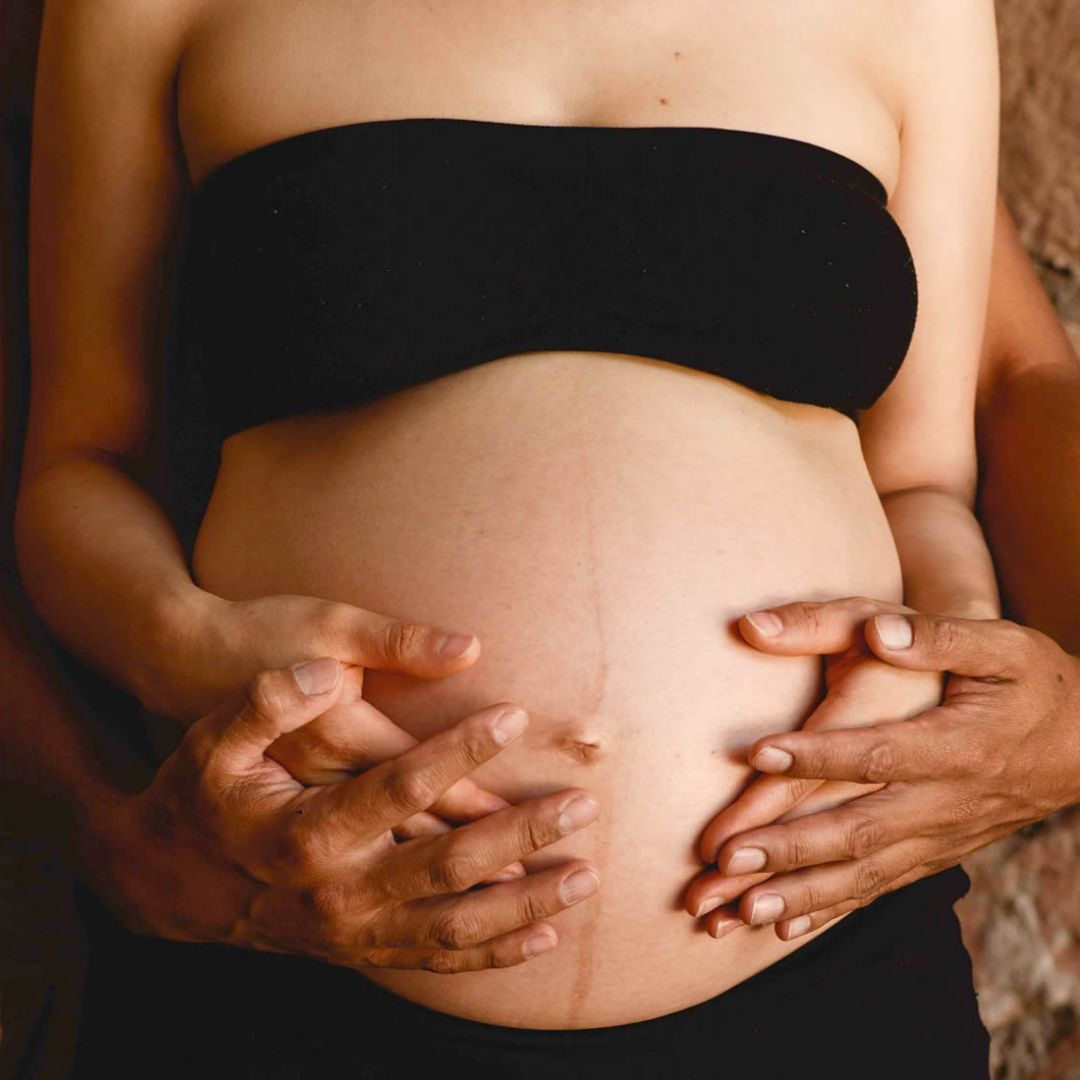Imagen de una mujer embarazada sentada en el suelo: Mujer embarazada sentada en el suelo con una mano en su vientre, simbolizando la preparación y conexión emocional durante el embarazo.